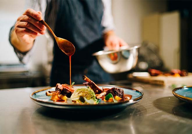 Chef finishing a dish with sauce using fresh local ingredients in a pub kitchen